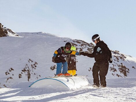 A boy is practicing snowboarding on a snowy hill. A coach is assisting him in a winter landscape.