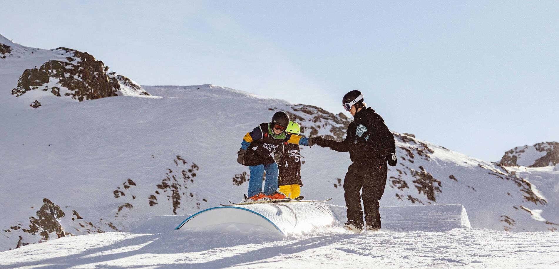 A boy is practicing snowboarding on a snowy hill. A coach is assisting him in a winter landscape.