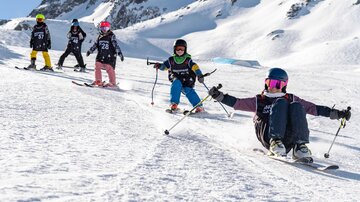 A group of children is skiing in a snowy mountain range. They are wearing bright ski clothing and enjoying the day on the slopes.