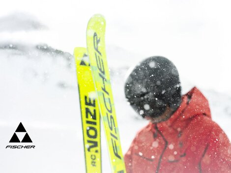 A skier is standing in the snow with yellow skis. The surroundings are wintry and covered with snow.