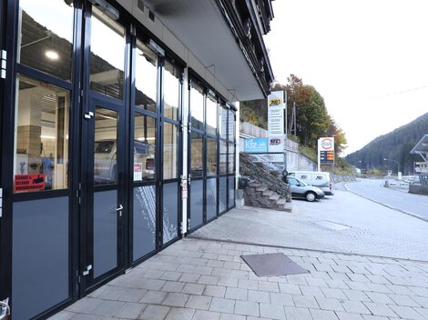 A modern business building with large windows and smooth stone slabs. In the background, mountains and a quiet street can be seen.