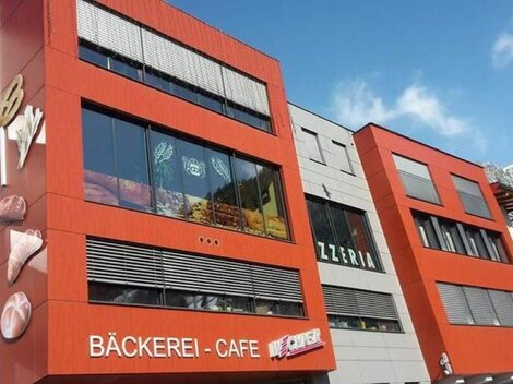 A modern building with a striking red facade. On the ground floor, there is a bakery and a café.