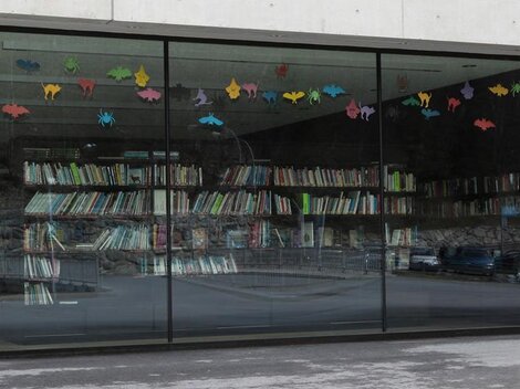 A modern window with colorful animal motifs that looks out onto a wall of books. The books are neatly arranged on shelves.