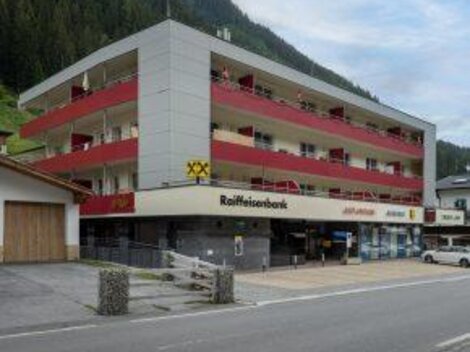 A modern building with several floors and balconies.  
At the bottom, there is a Raiffeisen bank and shops.