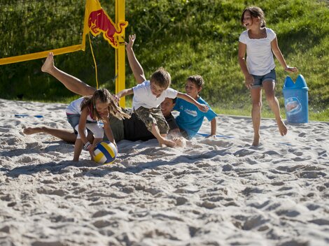 A group of children is playing beach volleyball in the sand. Two children are laughing as they struggle for the ball.