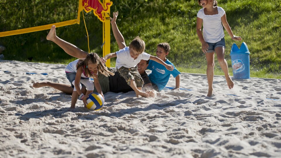 A group of children is playing beach volleyball in the sand. Two children are laughing as they struggle for the ball.