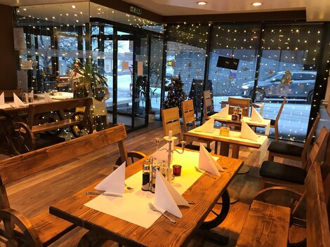 A cozy restaurant with wooden tables and chairs. Large windows reveal Christmas decorations and atmospheric lighting.