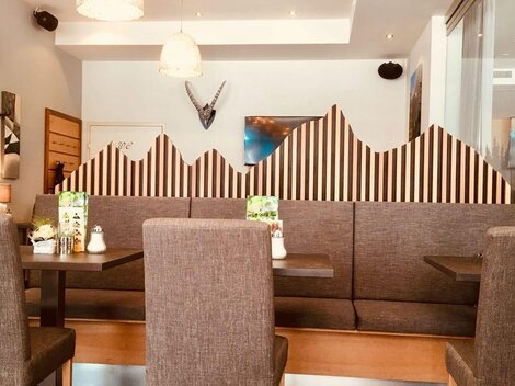 A modern restaurant with cozy seating areas and a decorative mountain-themed wall. The light is bright and friendly, creating an inviting atmosphere.