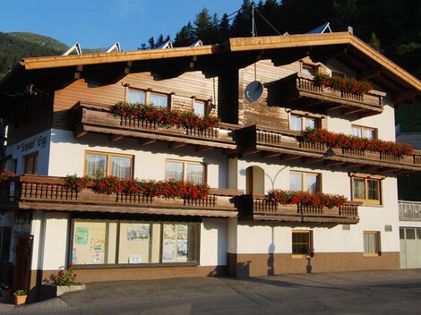 A traditional wooden building with many balconies adorned with red flowers. In the background, green mountains can be seen.