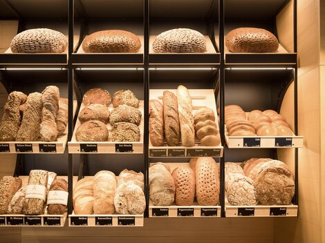 A selection of fresh bread in various shapes and colors. The breads are neatly arranged on shelves.