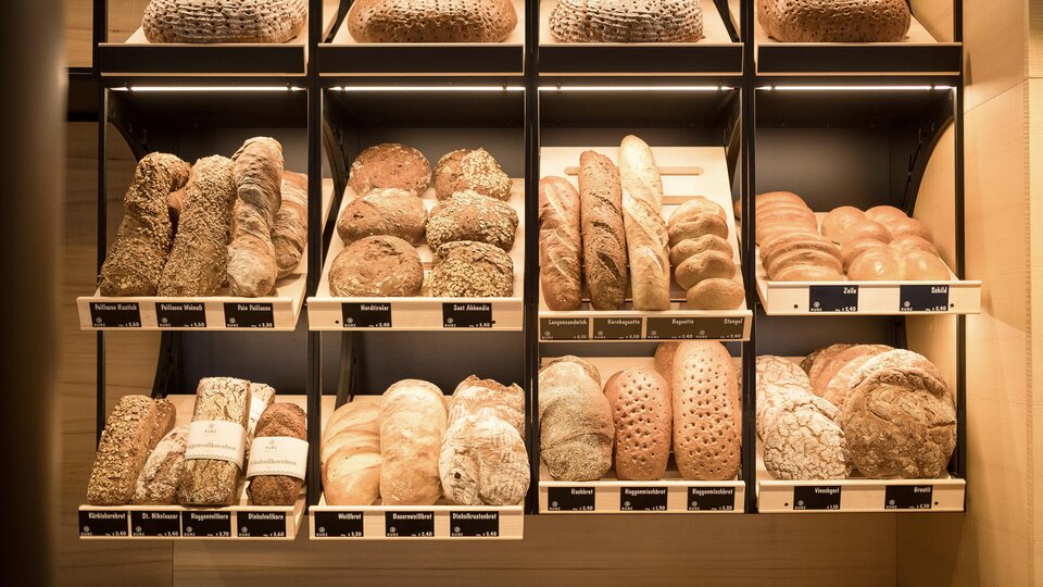 A shelf full of fresh breads in various shapes and sizes. The breads are neatly arranged and offer a selection of different types.