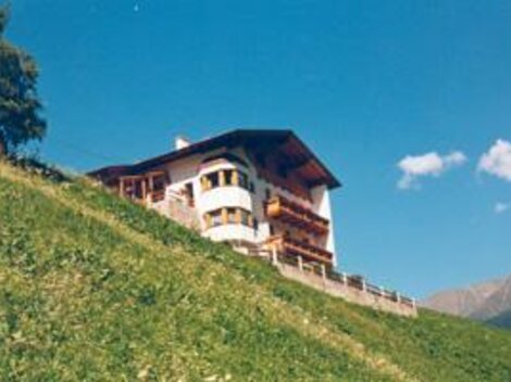A beautiful house on a hill, surrounded by green meadows. The sky is blue with a few clouds.
