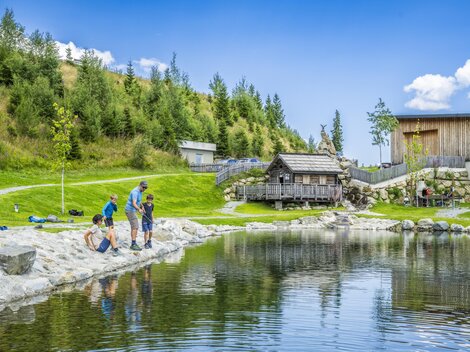 A tranquil lake surrounded by green meadows and trees. Children and adults enjoy nature and spend time by the shore.