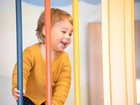 A cheerful child is playing on a playground device. They are wearing a yellow sweater and smiling happily.