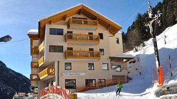A cozy hotel in the mountains with a snow-covered slope. In the background, trees and a clear sky can be seen.