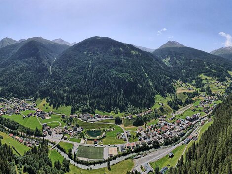 A beautiful panoramic view of a valley surrounded by high mountains. The landscape is green with forests and a small village in the background.