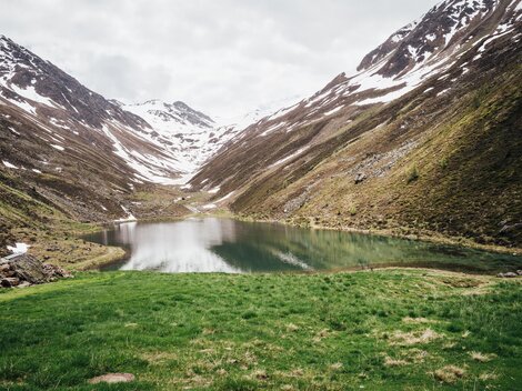 A tranquil mountain lake surrounded by snow-covered mountains. The landscape is green and idyllic.