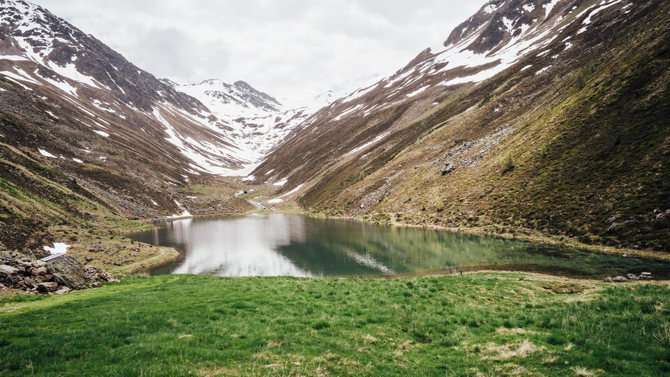 A tranquil mountain lake surrounded by snow-covered mountains. The landscape is green and idyllic.