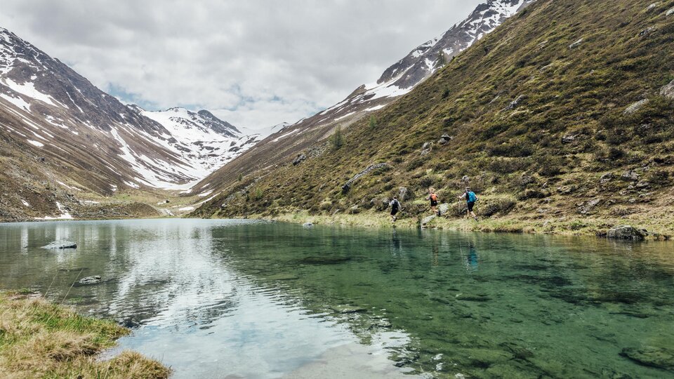 A quiet lake in the mountains, surrounded by snow-capped peaks. Hikers stand by the shore and enjoy nature.