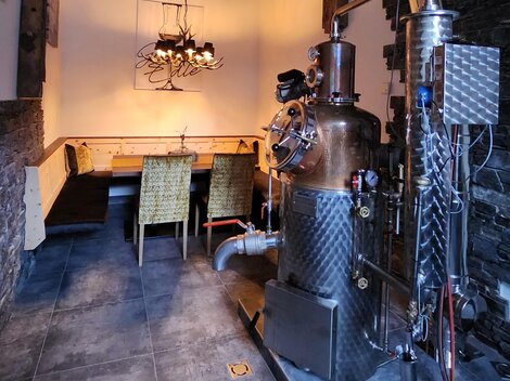 A cozy room with a large distillation device. In the background, several chairs are arranged around a table.