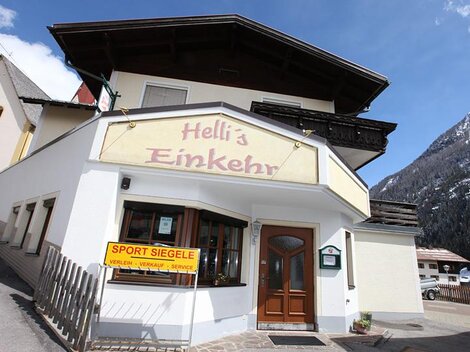 A cozy inn called "Hell's Einkehr" in the mountains. The facade is designed in a friendly manner and there is a view of the surrounding mountains.