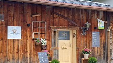 A rustic wooden building with an inviting front door. Flowers and plants adorn the entrance area, and a sign indicates that the business is open.