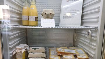 A refrigerator with various food items, including bottles of drinks, eggs, and several packaged foods. On the upper shelf, there is a sign with information.