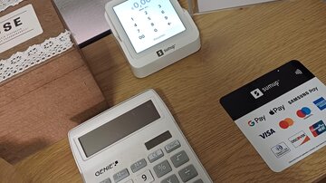 A table with a cash register and a payment terminal. Next to it lies a card with various payment methods.