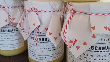 Three jars of clarified butter, decorated with paper and a red ribbon. The labels contain information about the product and the expiration date.