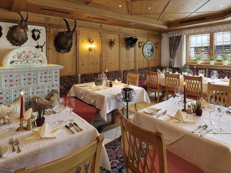 A cozy restaurant with wooden walls and elegant tablecloths. The tables are festively arranged, and the decoration includes traditional hunting trophies.