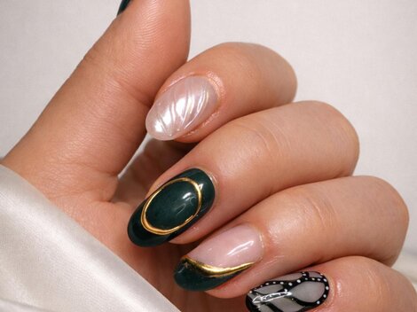 A hand with artistically designed nails in various colors. The nails are adorned with golden and black details.