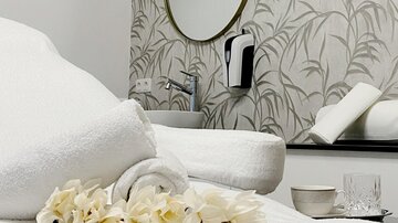 A relaxing wellness area with fresh towels and decorative flowers. In the background, a round mirror and a stylish wall design can be seen.