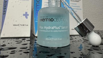 A liquid skin serum in a glass bottle is in the foreground. In the background, other skincare products in elegant packaging can be seen.