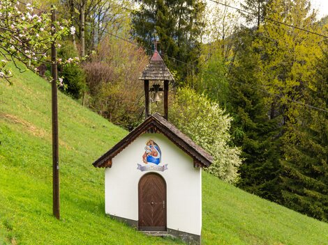 A small chapel stands on a green meadow. Surrounded by trees, it conveys a quiet and idyllic atmosphere.