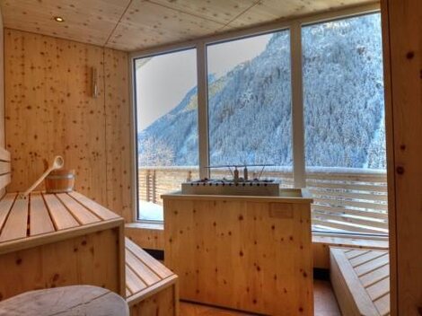 A cozy wellness area made of wood with a view of snow-covered mountains. Light streams through large windows, creating a relaxing atmosphere.