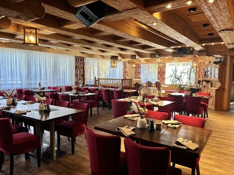 A cozy restaurant with wooden elements and red chairs. The tables are set warmly and the windows offer a view outside.