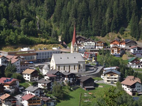 A picturesque mountain town with traditional houses and a distinctive church. Surrounded by green meadows and dense forests.