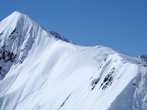 A snow-covered mountain under a clear blue sky. The landscape is majestic and impressive.