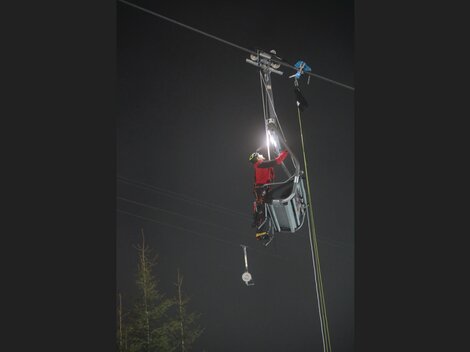 A person is working on a cable car at night. They are wearing safety gear and using a flashlight.