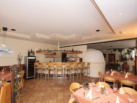 A cozy restaurant with a bar and wooden furniture. The tables are elegantly set and there is a beautiful indoor area.