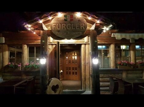 A rustic wooden restaurant with an inviting facade and warm lighting. The entrance door is made of wood and the windows are adorned with blooming plants.