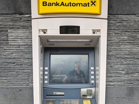 An ATM on a wall. It displays a simple user interface with a card and a screen.