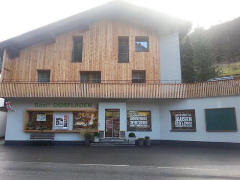 A traditional village shop with a wooden facade and an inviting entrance front. In front of the shop are advertising posters for local products and specialties.