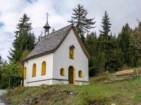 A small, white chapel stands amid trees. The sky is cloudy and the surroundings are green. | © Bernhard Gruber – Photography