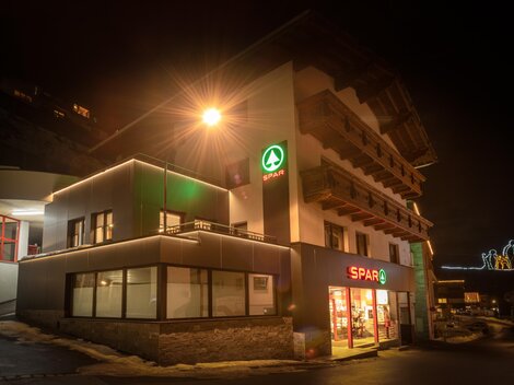 A store with bright lights at night. It is a SPAR market in a modern building.