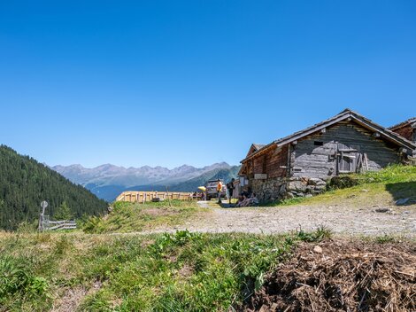 A picturesque mountain village with traditional wooden buildings and a beautiful view of the mountains. The bright blue sky and the green meadow give the scene a serene atmosphere.