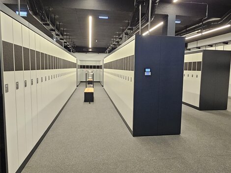 A modern locker room with many white lockers. The walls are gray and the floor is carpeted.