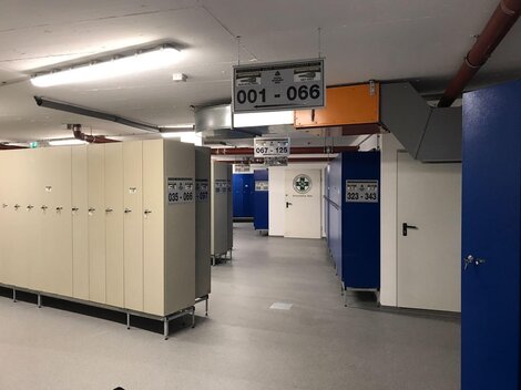 A modern changing area with lockers and spacious corridors. The walls are painted in blue and beige, and there are several number plates.