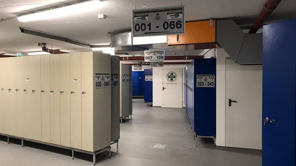 A modern changing area with lockers and spacious corridors. The walls are painted in blue and beige, and there are several number plates.