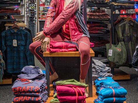 A display window with a mannequin showcasing sportswear by Craft. In the background, additional clothing items and accessories are arranged.